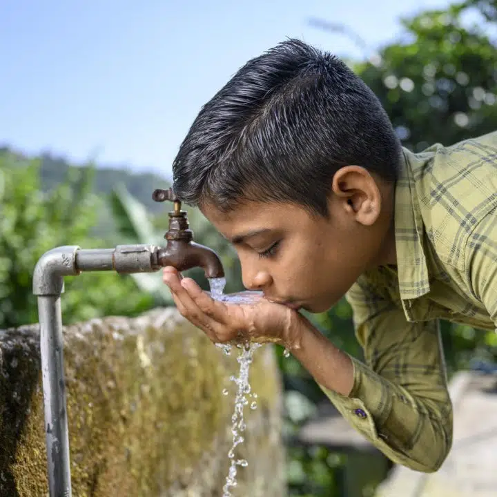 Un enfant heureux qui boit de l'eau à partir d'une source d'eau courante fournie à son village par JJM. Lieu : Village Bathol, Solan, Himachal Pradesh, Inde. © UNICEF/UN0718845/Panjwani