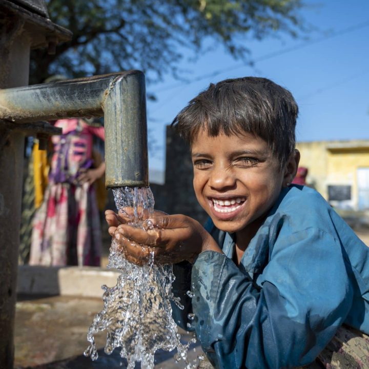 Photo d'un jeune garçon heureux d'avoir accès à la pompe à eau du village Mata Devi, Abu Road, Rajasthan, en Inde. © UNICEF/UN0389249/Panjwani