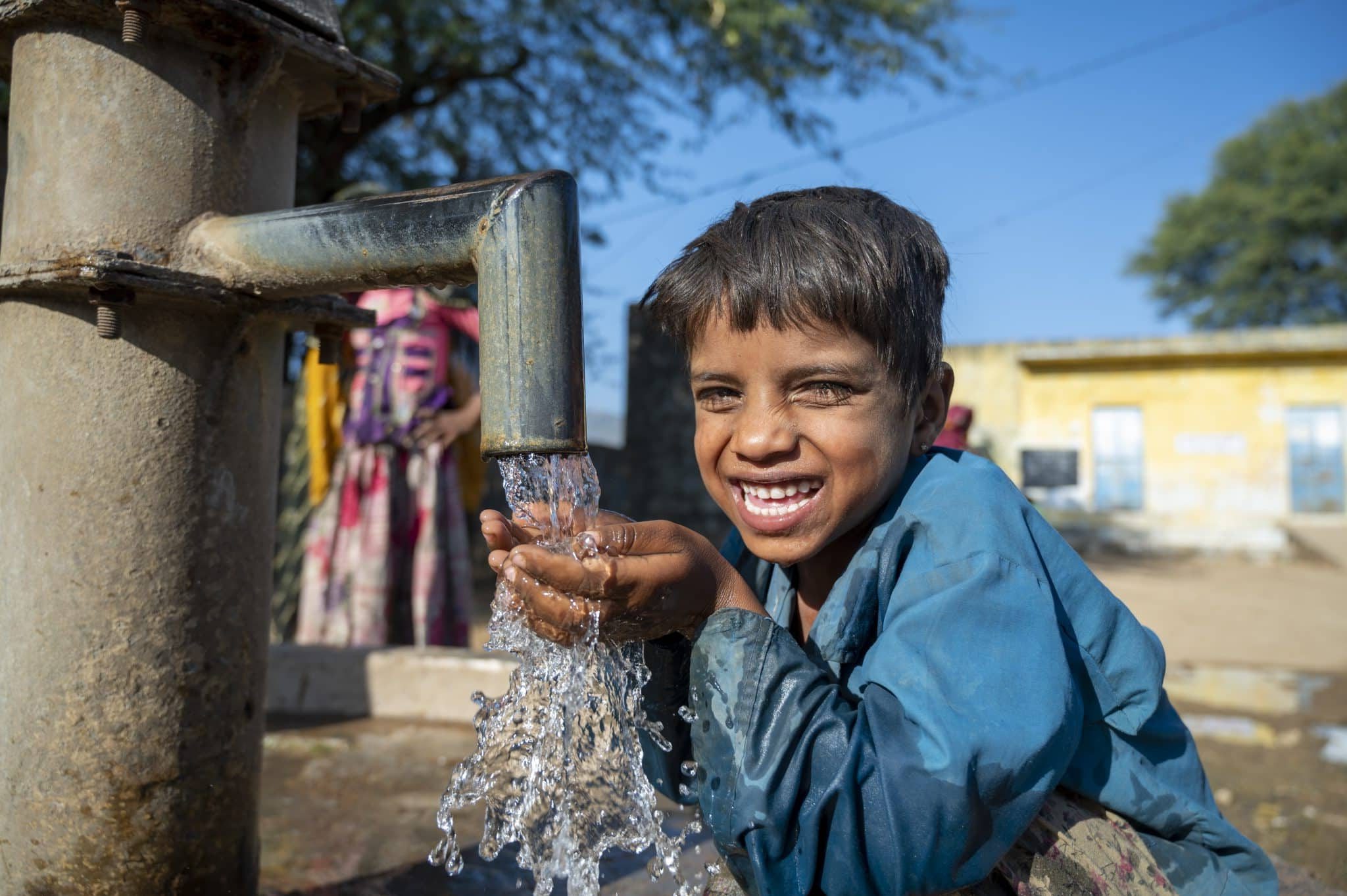 Photo d'un jeune garçon heureux d'avoir accès à la pompe à eau du village Mata Devi, Abu Road, Rajasthan, en Inde. © UNICEF/UN0389249/Panjwani