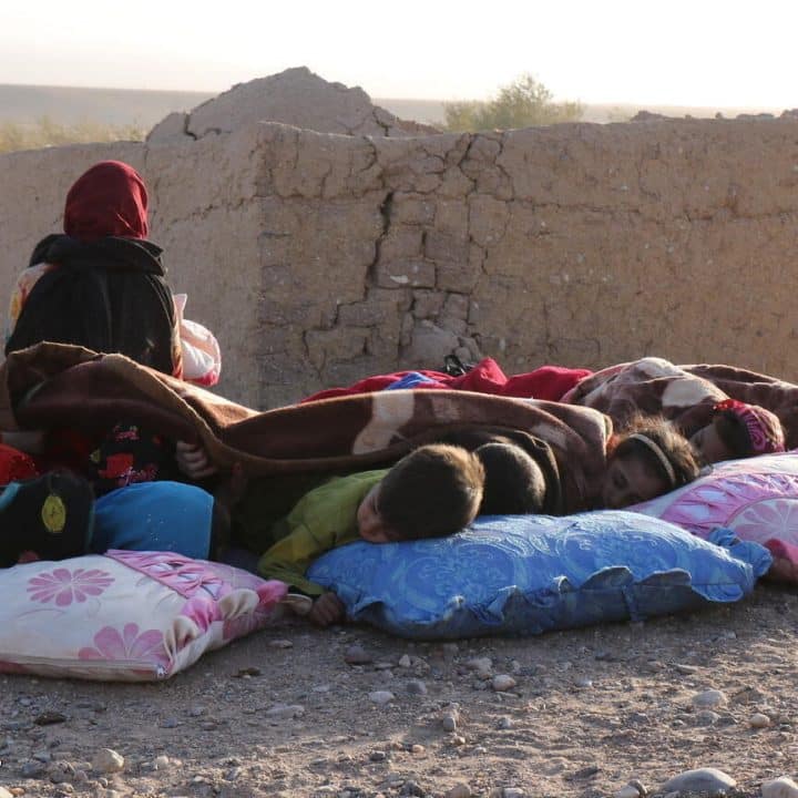 Des enfants afghans se reposent sous une couverture à côté de maisons endommagées, après le tremblement de terre dans le village de Sarbuland du district de Zendeh Jan dans la province d'Hérat le 7 octobre 2023 (Photo par Mohsen KARIMI / AFP). © UNICEF/UNI448658/Karimi AFP