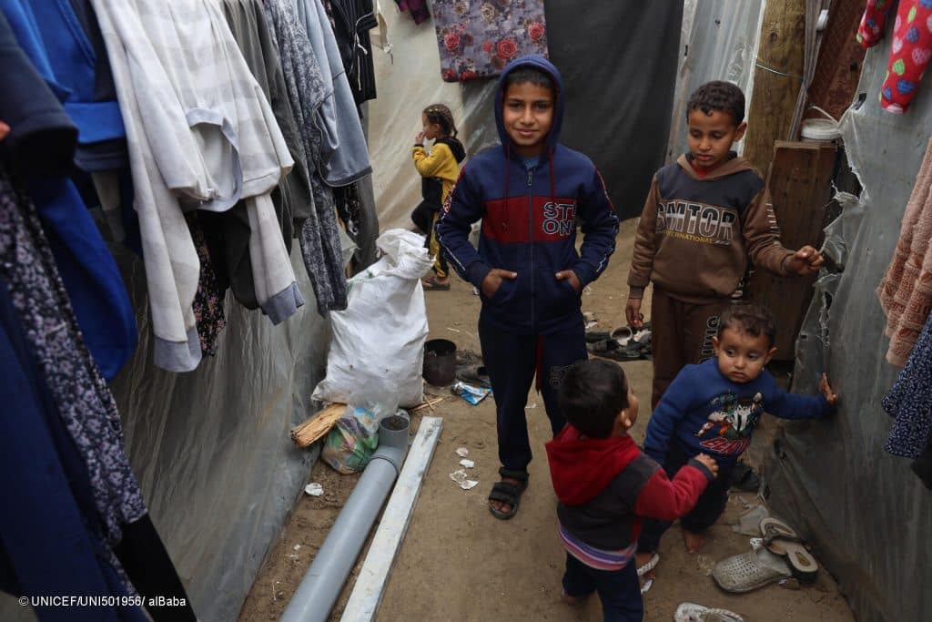 Le 11 janvier 2024, Abedalrahman, 13 ans, au centre se tient avec d'autres enfants à côté de tentes dans un centre d'hébergement situé près de l'université Al-Aqsa dans la bande de Gaza. © UNICEF/UNI501956/ alBaba