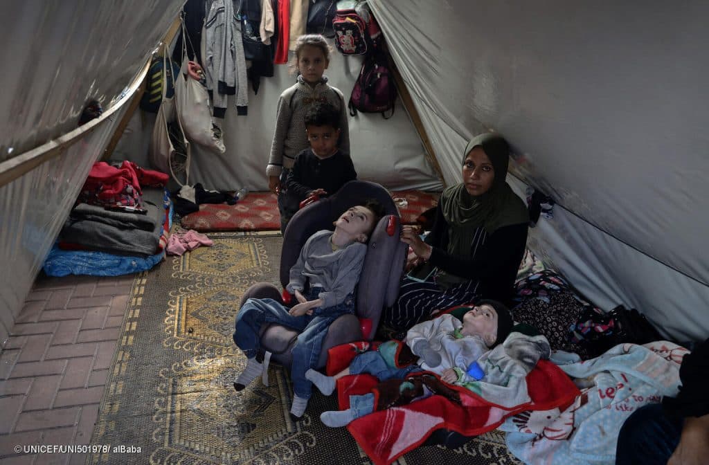 Le 11 janvier 2024, Mena, une mère déplacée, pose pour une photo avec ses enfants dans une tente à l'intérieur de l'université d'Al-Quds dans la bande de Gaza. © UNICEF/UNI501978/ alBaba