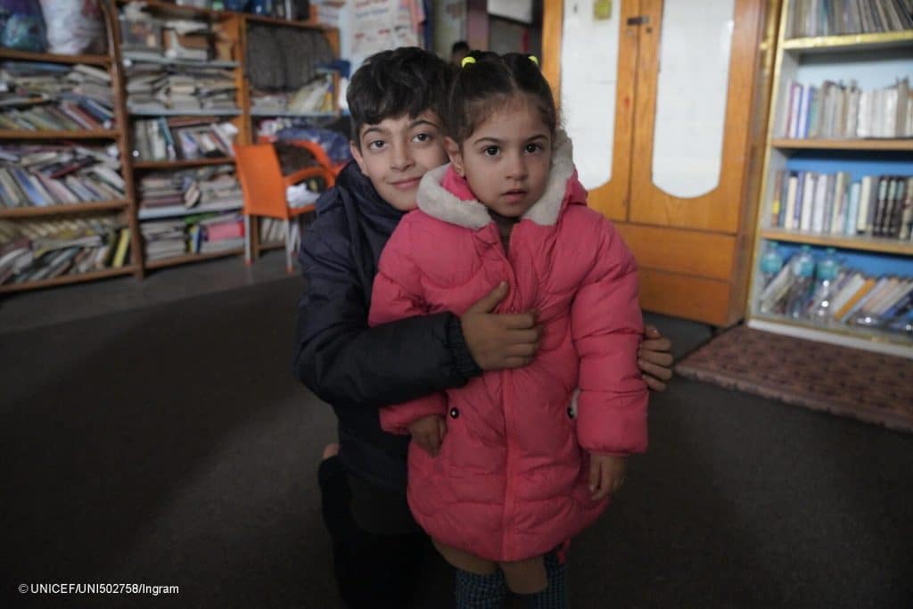 Le 13 janvier 2024, Ahmed, 10 ans, et Suha, 3 ans, posent pour une photo au Centre des femmes de Rafah, dans le sud de la bande de Gaza, actuellement utilisé comme abri, après la distribution de manteaux d'hiver, achetés par l'UNICEF et distribués par les partenaires de l'UNICEF. © UNICEF/UNI502758/Ingram