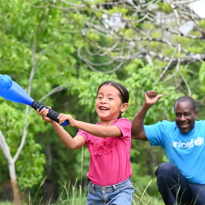Un membre du personnel de l'UNICEF joue au baseball avec Oneida, 5 ans, dans le village d'Otoxha, au sud du Belize. Sur place, l'UNICEF a mis en place un programme de protection sociale. © UNICEF/UNI594461/Dejongh